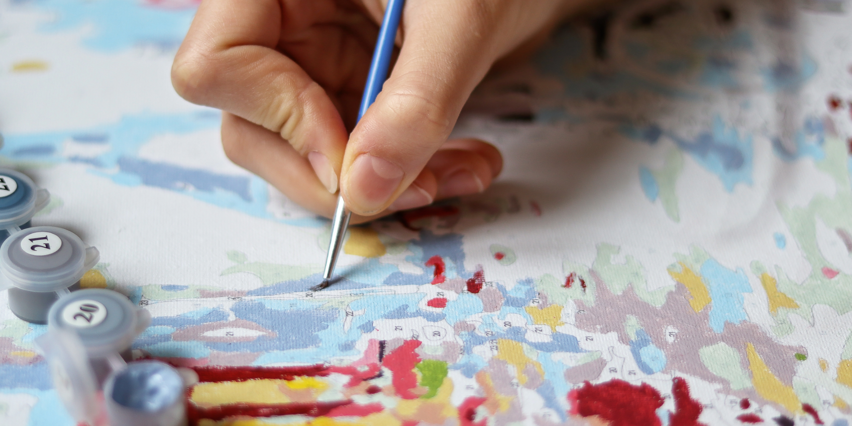 An image of a person's image holding a paintbrush and coloring in a paint by numbers painting.