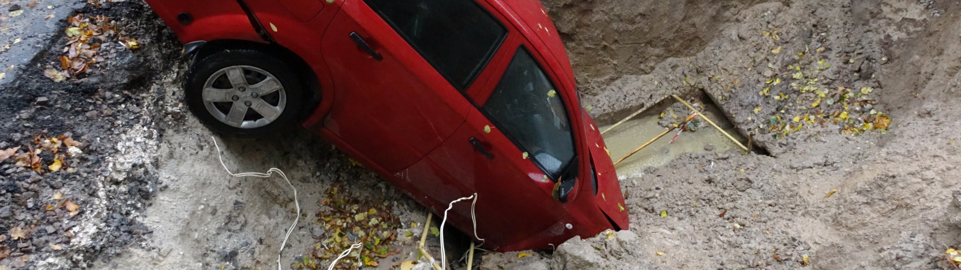 A car partially sunken into a large pothole on a dirt road.