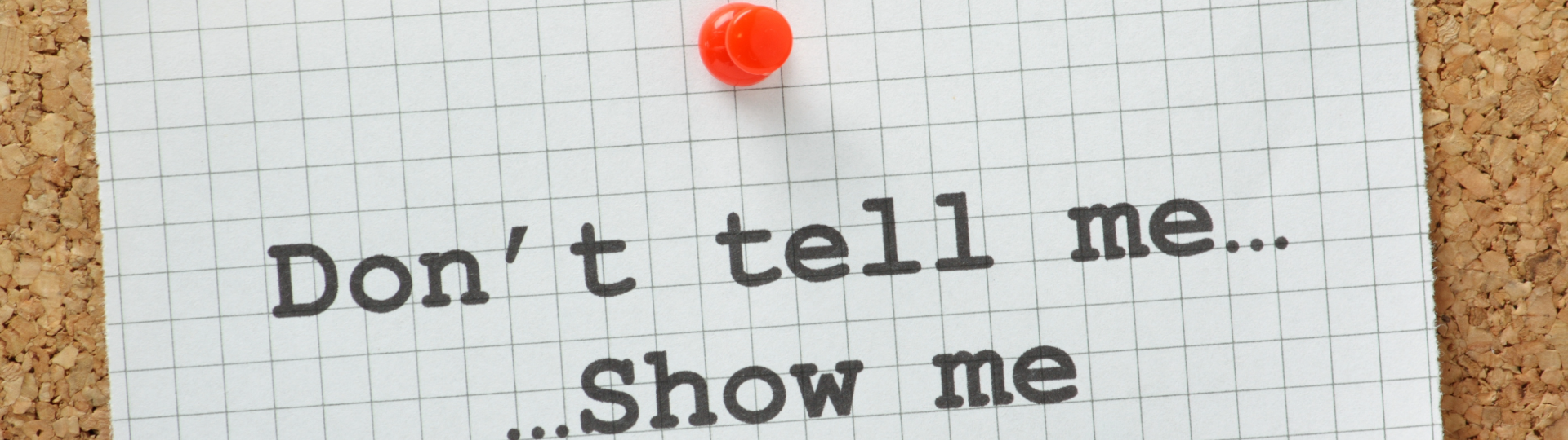 A note with the words "Don't tell me... Show me" is pinned to a corkboard with a red pushpin.