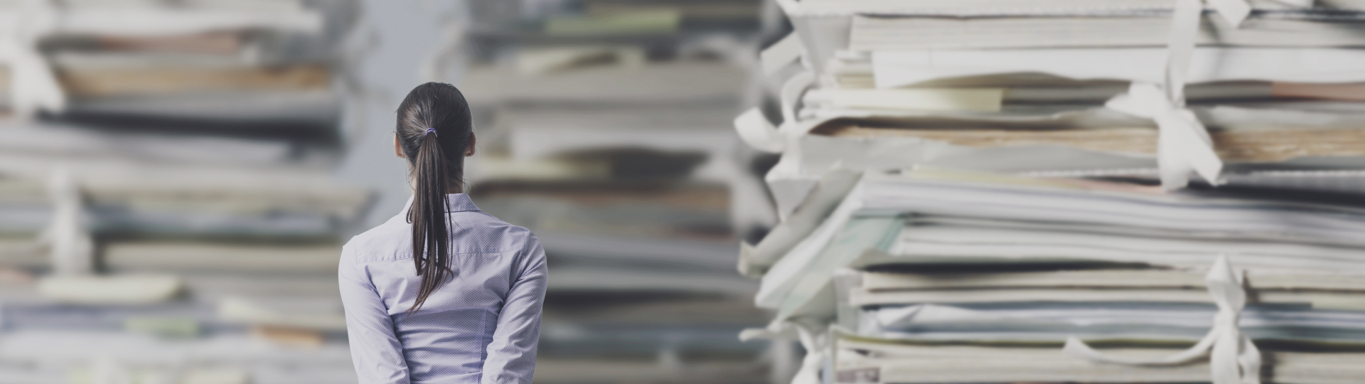 A woman facing large stacks of paper and documents, symbolizing an overwhelming amount of information.