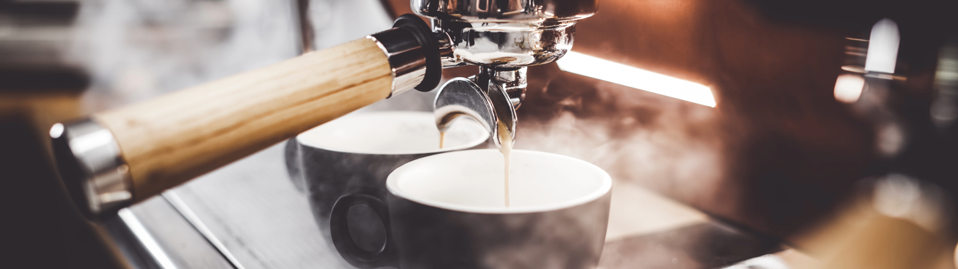 Close-up of an espresso machine brewing fresh coffee into two cups, with steam rising around them.