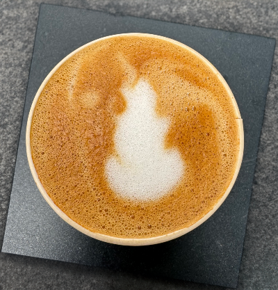 A close-up of a cup of almond macchiato with a heart-shaped foam design on top of the coffee.