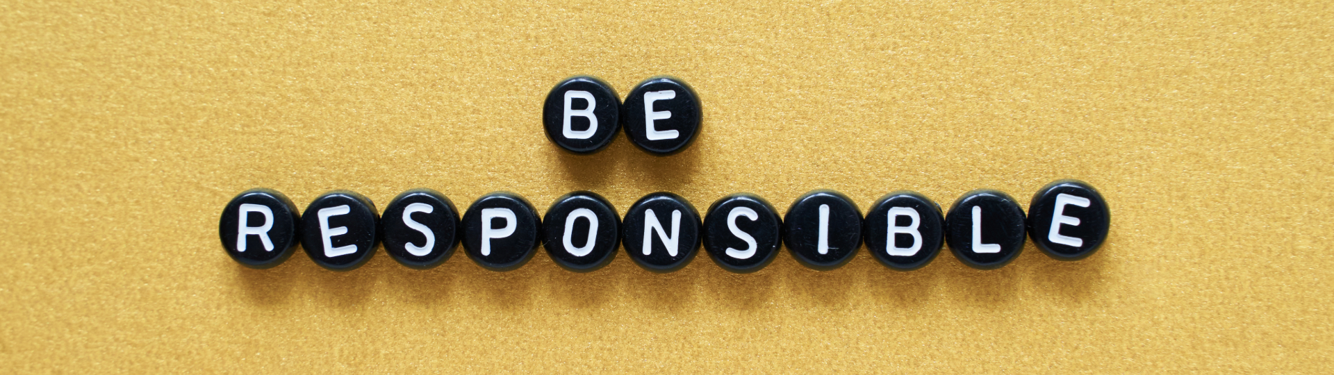 The phrase "Be Responsible" spelled out with black round letter beads on a textured yellow background.