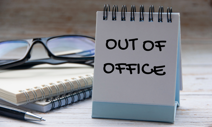 An image of an "Out of Office" placard sitting on a desk.
