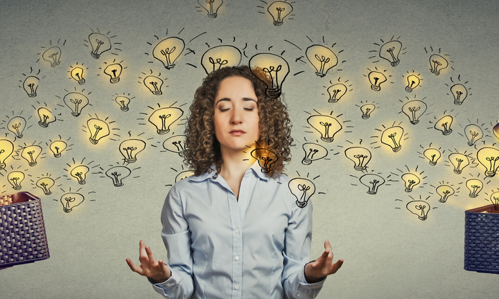 A woman with curly hair is meditating with closed eyes, surrounded by glowing lightbulb illustrations.